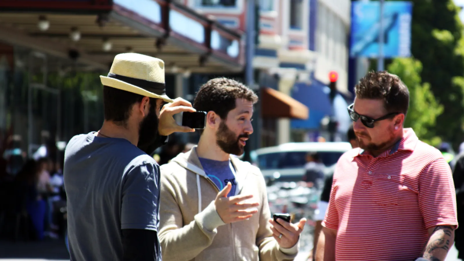 Three men standing talking on a city street, one gesturing mid-sentence while the others listen.
