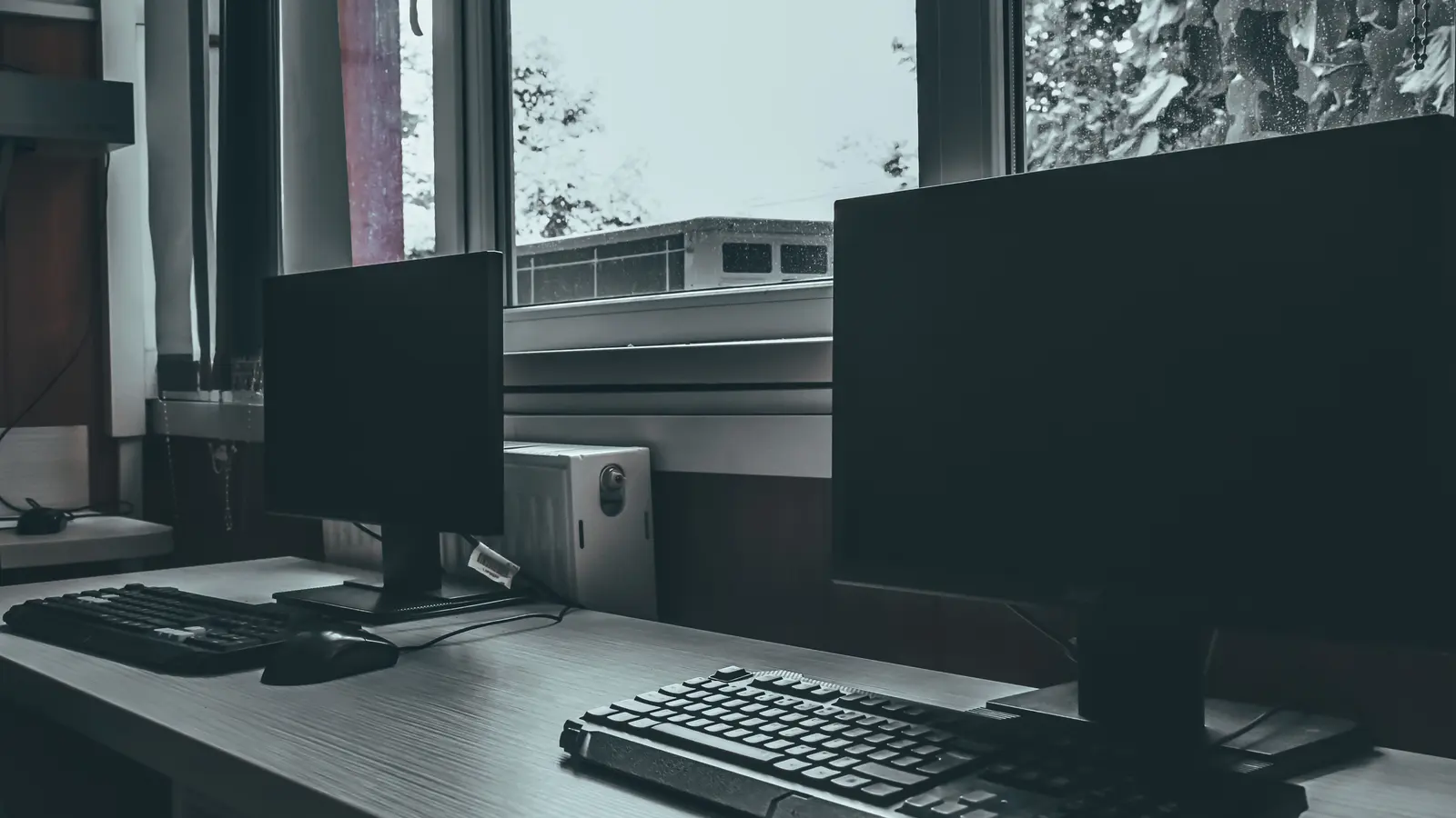 Workstations with switched-off monitors beside a bright window in a quiet, empty office.