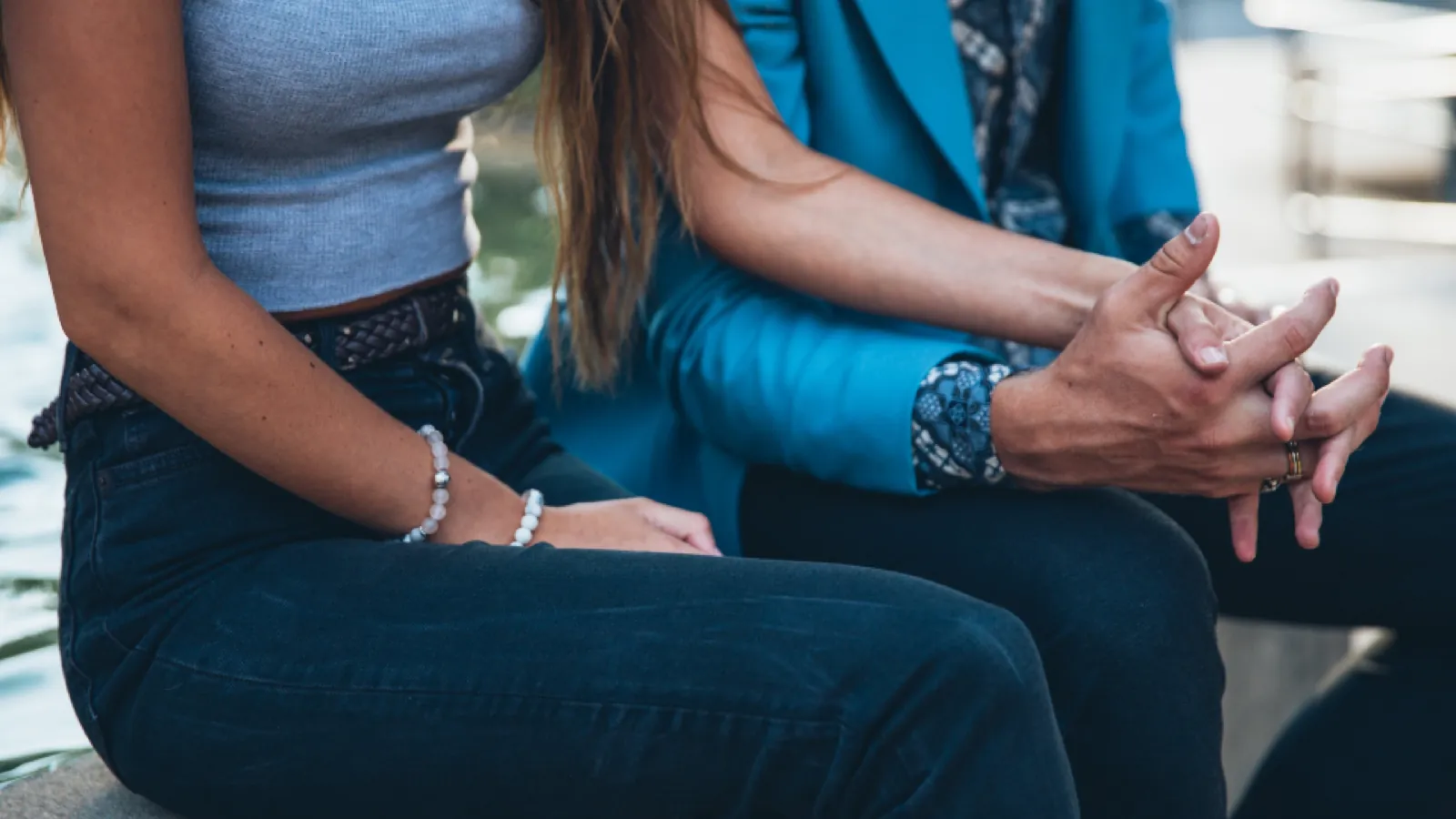 Two people sitting close together on a sofa, cropped at the waist, hands clasped in their laps mid-conversation.