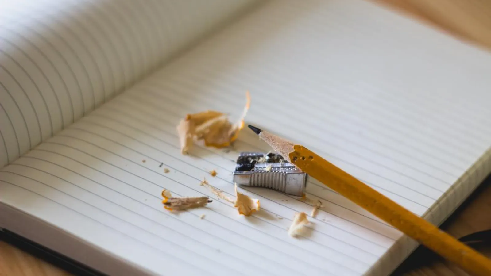 A lined notebook page with a yellow pencil lying across it and pencil shavings scattered over the paper.
